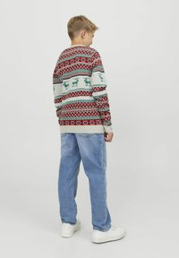 Rode, groene en witte gebreide trui met rendiermotieven en geometrische ontwerpen, gedragen met lichtblauwe jeans en witte sneakers.