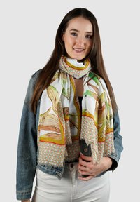 Veelgekleurde zijden sjaal met een bloem- en geometrisch patroon, met groene en gele accenten, om de nek van een persoon gedrapeerd.