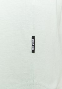 Helles grünes Sweatshirt aus weichem Stoff mit glatter Textur und einem schwarzen Etikett mit "ONLY & SONS" an der Seitennaht.