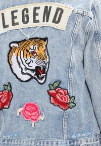 Giacca di jeans con un patch "LEGEND", che presenta una testa di tigre feroce e tre rose ricamate in tonalità di rosso e rosa.