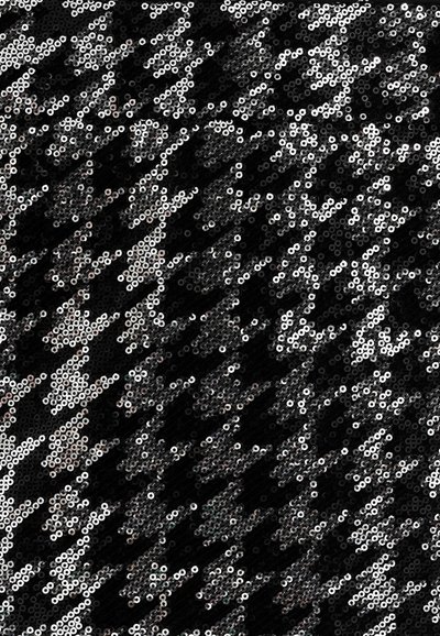 Tessuto nero ricoperto di paillettes argentate circolari disposte in un motivo diagonale, creando una superficie testurizzata e riflettente.