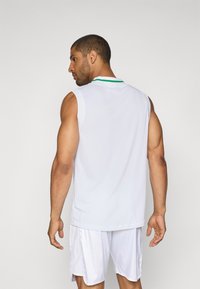 Weißes sportliches ärmelloses Shirt mit grünem Kragen und strukturiertem Stoff, kombiniert mit weißen Shorts, die die Rückansicht des Outfits zeigen.