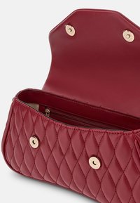 Rode gewatteerde handtas met gouden drukknoopsluitingen, open flap en zichtbare binnenritszak tegen een witte achtergrond.