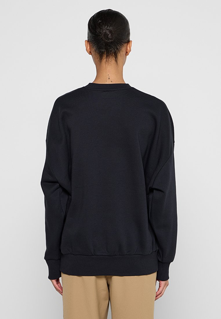 Schwarzer Pullover mit Rundhalsausschnitt, überschnittenen Schultern und elastischen Bündchen. Weiche Textur, lässige Passform und geripptes Saumdetail.