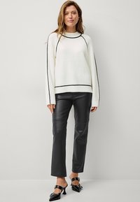 Maglione bianco a maglia con dettagli neri, caratterizzato da un collo rotondo e maniche lunghe, abbinato a pantaloni di pelle neri e mule con tacco neri.