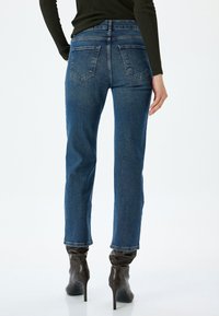Vaqueros de mezclilla azul oscuro, con una cintura alta, piernas rectas y cinco bolsillos. Combinados con botas de tacón marrones.