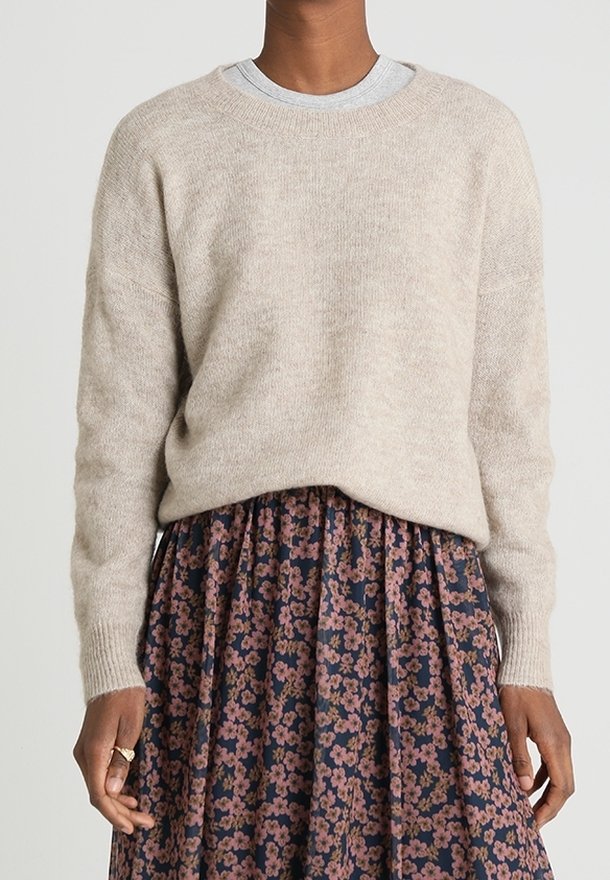 Personne portant un pull en maille beige sur une chemise grise et une jupe plissée bleu marine avec un motif floral rose.