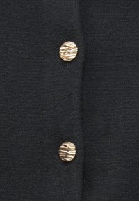 Černý pletený kardigan s dvěma texturovanými knoflíky ve zlaté barvě. Látka je měkká a má hladký, mírně elastický povrch.