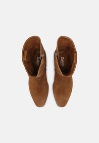 Bruine suède enkelboots met een spitse neus, zijrits en een gladde textuur. Voorzien van een zachte binnenvoering met zichtbaar merkembleem.