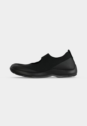 Zapato negro sin cordones con suela flexible, puntera redondeada y recorte lateral, diseñado para comodidad y uso casual.