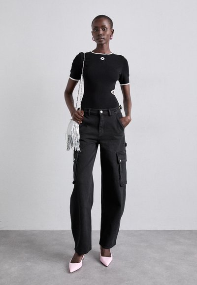 Top negru mulat cu detalii albe și o decupare, asortat cu pantaloni cargo negri largi cu buzunare și pantofi cu vârful punctat roz. Accesorizat cu o geantă mică albă cu franjuri.