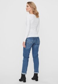 Witte lange mouwen top gecombineerd met high-waisted blauwe jeans, met een ontspannen pasvorm en opgerolde mouwen, gedragen met zwarte enkellaarsjes.