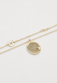 Pulseira de corrente dourada com um pendente circular com texto em relevo. A corrente é ligada, com um fecho de lagosta para prender.