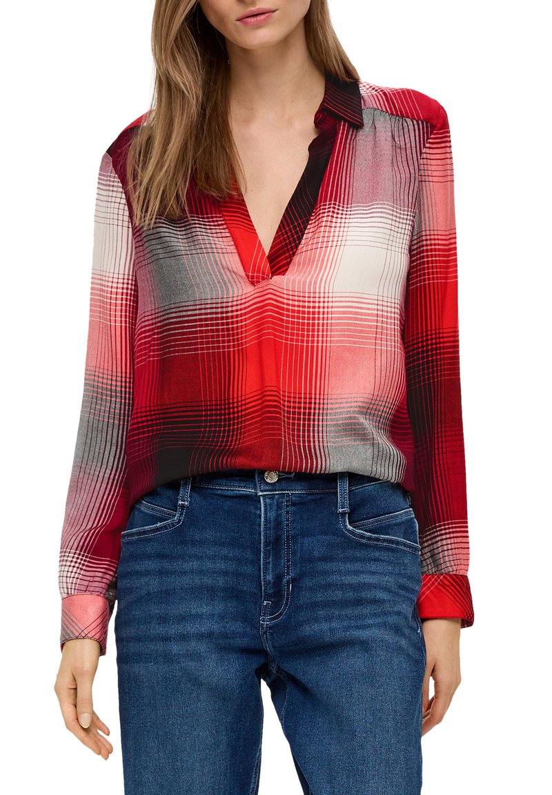 Blusa a quadri rossi e grigi con scollo a V, maniche lunghe e polsini, abbinata a jeans in denim blu. Tessuto liscio con una leggera lucentezza.