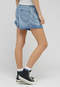 Vaaleansiniset farkkushortsit, joissa on käännetty helma, sisältävät kaksi takataskua ja kontrastiväriset tikkausomitukset. Yhdistetty mustiin lenkkareihin ja valkoisiin sukkiin.