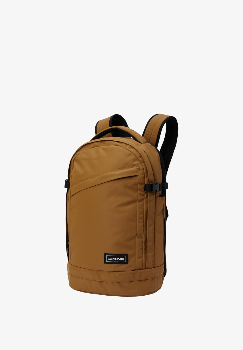 Hnědý látkový batoh s hladkým povrchem, má nastavitelné popruhy, přední kapsu na zip a černou logovou nášivku na spodní straně.