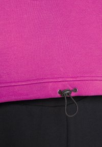 Top rosa de manga corta con acabado texturizado, con un cordón ajustable en el dobladillo y combinado con pantalones negros.