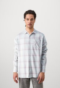 Light blue plaid shirt made of soft fabric, featuring long sleeves, a button-up front, and a single front pocket with diagonal pattern accents.