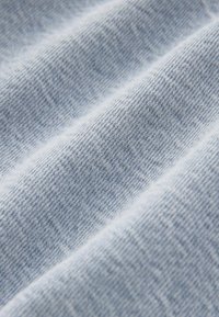 Tissu en denim bleu clair avec un tissage texturé, présentant des variations subtiles de couleur et de motif sur la surface, créant une apparence douce.