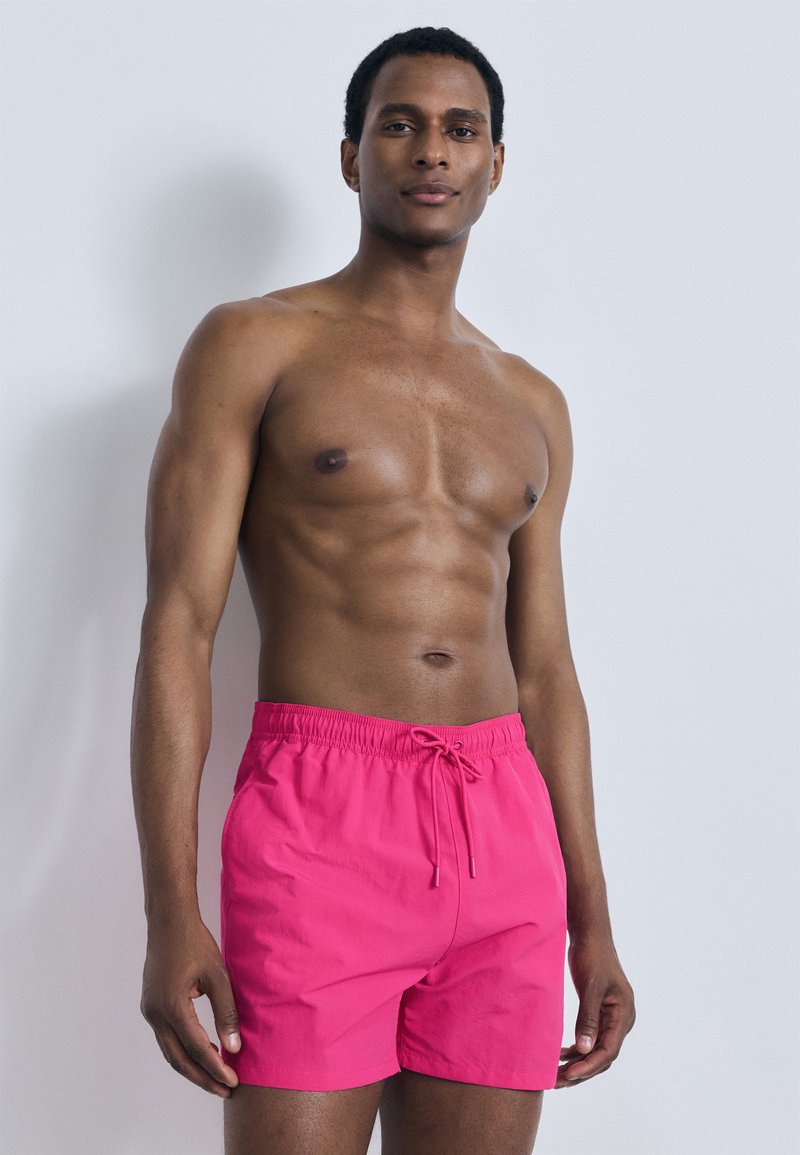 Ροζ μαγιό σορτς με ελαστική μέση και ρυθμιζόμενο κορδόνι. Ομαλό ύφασμα, μήκος πάνω από το γόνατο, με μινιμαλιστικό σχεδιασμό.