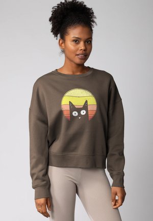 Donkergroen sweatshirt met een ronde kattenafbeelding, featuring gele en oranje zonsondergangkleuren. Ribgebreide manchetten en een ontspannen pasvorm.
