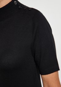 Pulover scurt negru cu mânecă scurtă și guler înalt, având un material texturat și patru accente cu nasturi pe umăr.