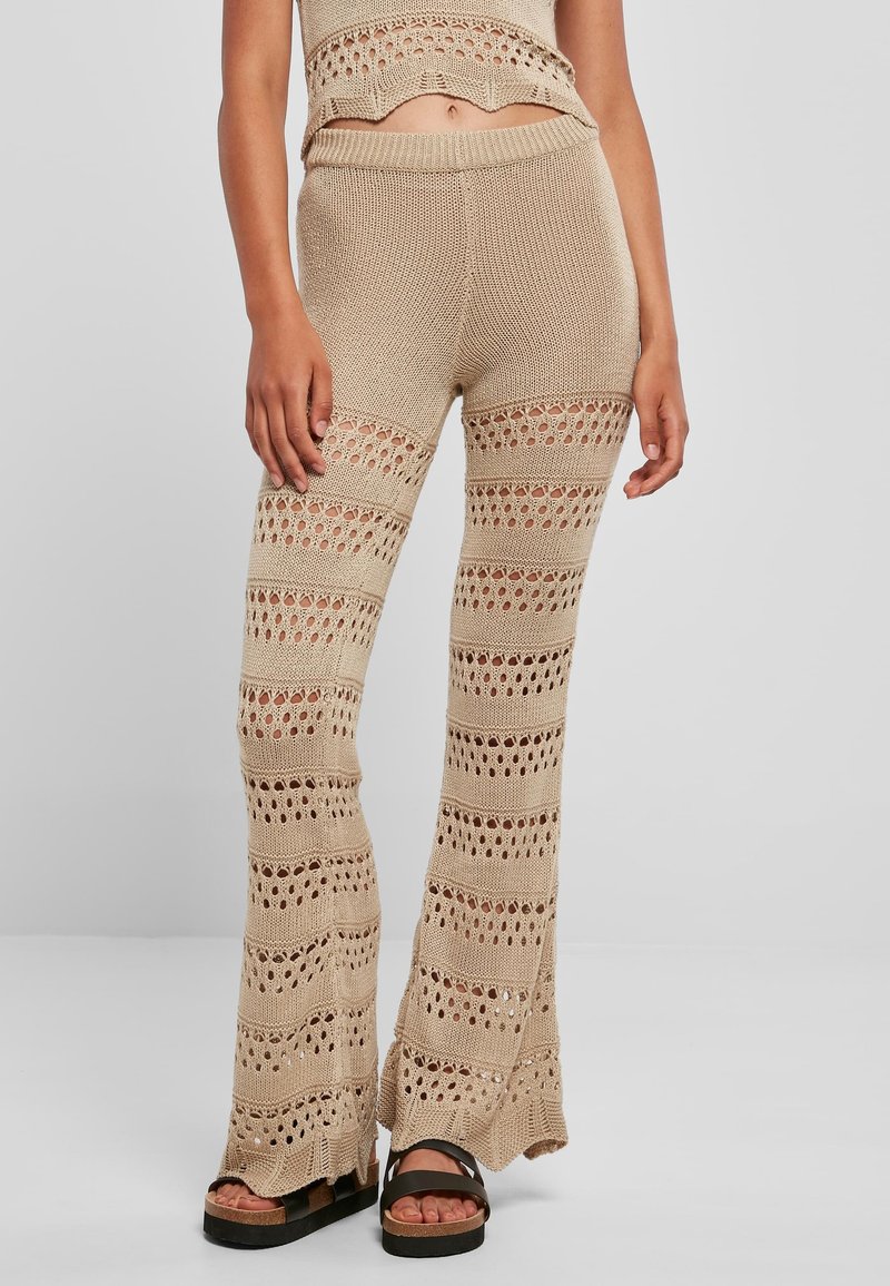 Pantalon beige en maille avec des rayures horizontales alternant entre mailles serrées et ajourées, assorti à un haut court et des sandales à plateforme noires.