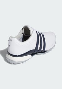 Bílé golfové boty s námořnickými akcenty, syntetický svršek, polstrovaná podešev, šněrovací design a texturované detaily na svršku a patě.