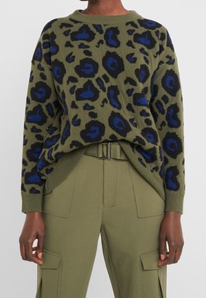 Pull vert olive avec imprimé léopard bleu et noir, associé à un pantalon cargo vert olive avec poches avant et ceinture.