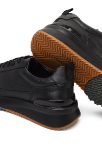 Zwarte sneakers met een bovenwerk van textuurleer, dikke zwarte rubberen zool en contrasterende gumzool. Heeft een afgerond ontwerp en subtiele accenten.