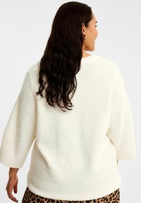 Hvid, struktureret sweater med trekvartærmer og rund halsudskæring, iført over en leopardprintet nederdel. Blødt, hyggeligt materiale.