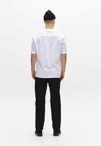 Chemise blanche à manches courtes avec un ourlet droit, associée à un pantalon noir et un bonnet en tricot noir. Tissu lisse et coupe décontractée.