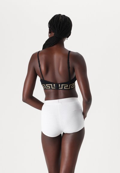 Black bra with a gold Greek key design, paired with white ribbed hipster shorts. Both have adjustable straps and a smooth texture.