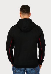 Felpa nera con cappuccio regolabile, inserti laterali rossi e maniche lunghe. La vista posteriore mostra una texture liscia e un design aderente.