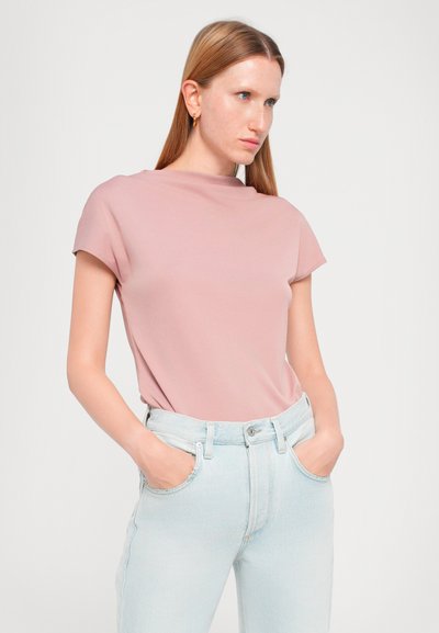 Top a maniche corte e collo alto in morbido tessuto rosa, abbinato a jeans high-waisted blu chiaro con chiusura classica a bottoni e tasche frontali.
