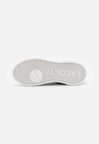 Semelle de chaussure en caoutchouc blanc avec un motif hexagonal, comportant un logo circulaire et des lignes parallèles pour la traction. Texture lisse et légère courbure.