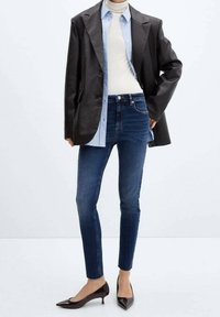 Blazer en cuir noir sur une chemise à boutons bleu clair, un col roulé blanc, un jean skinny en denim foncé et des escarpins à bout pointu noirs.