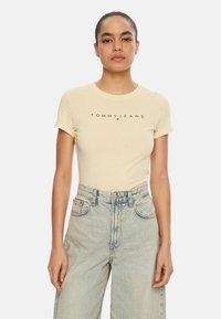 Camiseta de algodón amarilla con mangas cortas y cuello redondo, con texto "TOMMYJEANS" en negro en el pecho.