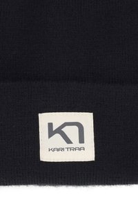 Stickad svart mössa med uppvikt kant, med en strukturerad finish. En rektangulär etikett med "KARI TRAA" och en logotyp är sydd på kanten.