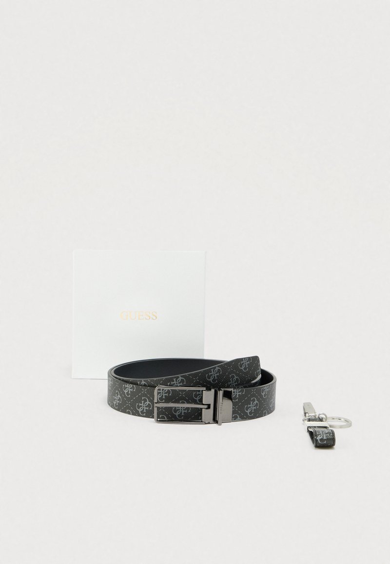 Zwart met patroon Guess-riem met metalen gesp, bijpassende sleutelhanger en witte Guess-doos met merk op een lichte achtergrond.