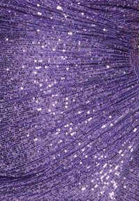 Tissu violet avec des paillettes créant une surface texturée et réfléchissante. Le matériau semble drapé avec des plis doux, ajoutant de la profondeur et de l'éclat.