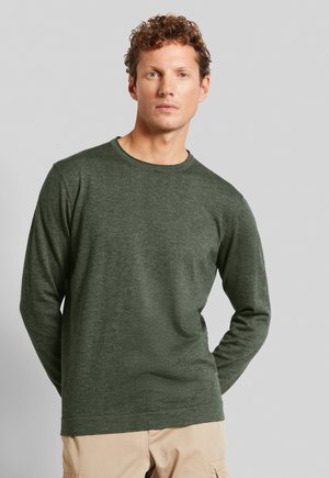 Long-sleeve green shirt made of textured fabric, featuring a crew neck and relaxed fit, paired with light beige pants.
