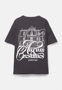 Šedé oversized tričko vyrobené z bavlny, s bílým grafickým designem domu a dekorativním textem na zadní straně.