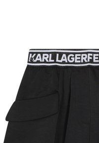 Shorts noirs avec une taille élastique, arborant un logo blanc. Comprend des poches latérales et un tissu léger et texturé.