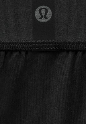 Musta kangas, jossa on sileä rakenne, sisältää rypistetyn helman ja pienen harmaan logon. Suunnittelu korostaa yksinkertaisuutta ja toiminnallisuutta.