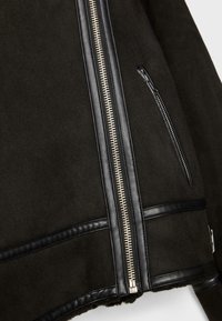Czarna zamszowa kurtka z skórzanymi akcentami, z zamkiem błyskawicznym z przodu i kieszenią na zamek. Miękka tekstura i zorganizowany krój.