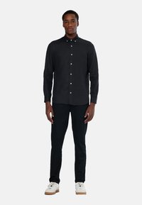 Mørk knap-op skjorte lavet af struktureret stof, med standard krave og slim fit, parret med sorte tapered bukser og hvide sneakers.