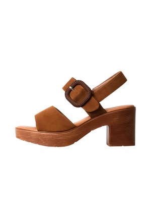 Sandalia abierta de ante marrón con tacón grueso de madera y hebilla cuadrada grande en la correa del tobillo, vista lateral sobre fondo blanco.