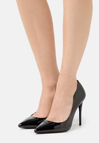 Escarpins noirs en cuir verni avec talons aiguilles, design à bouts pointus et silhouette élégante. Texture lisse avec une finition brillante.