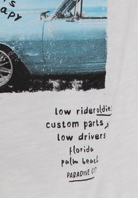 Gráfico de un coche vintage azul con texto abajo: "low rider oldies, piezas personalizadas, low drivers, Florida, Palm Beach, Paradise City."